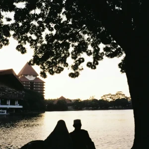 Dua orang sedang duduk di depan danau UI dan memandang salah satu gedung Universitas Indonesia dalam artikel Landmark di Kota Depok di website ecotown.id