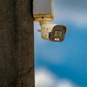 Kamera CCTV pengawas berwarna putih terpasang pada tiang dengan latar belakang langit biru dalam artikel "Cara Pasang CCTV Rumah" di website Ecotown.id