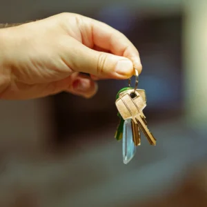 Tangan seseorang sedang memegang dan menyodorkan seikat kunci rumah dalam artikel "Waktu Terbaik Beli Properti" di website Ecotown.id