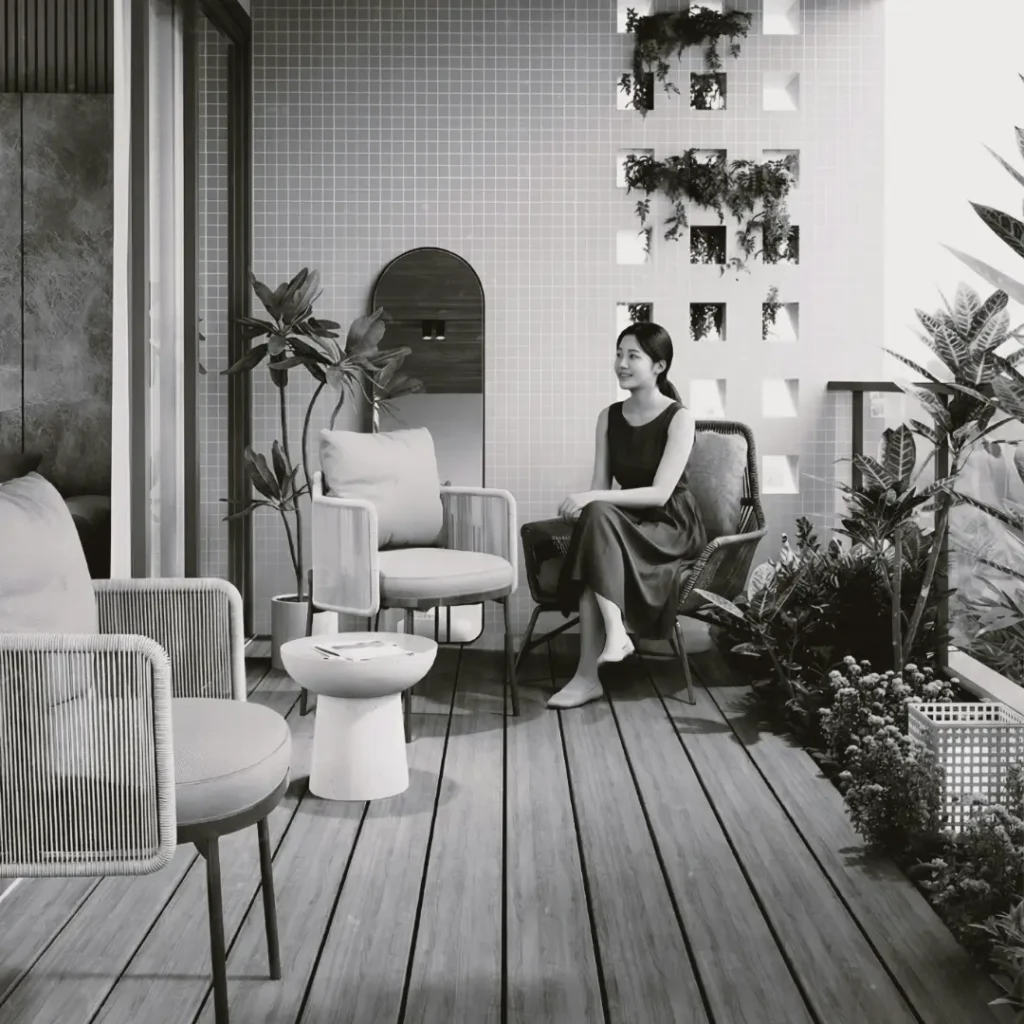 Seorang wanita duduk bersantai di area teras atau balkon rumah minimalis bertema monokrom yang dihiasi tanaman hijau dan kursi santai. Gambar ini berada dalam artikel "Desain Teras Rumah Minimalis" di website Ecotown.id