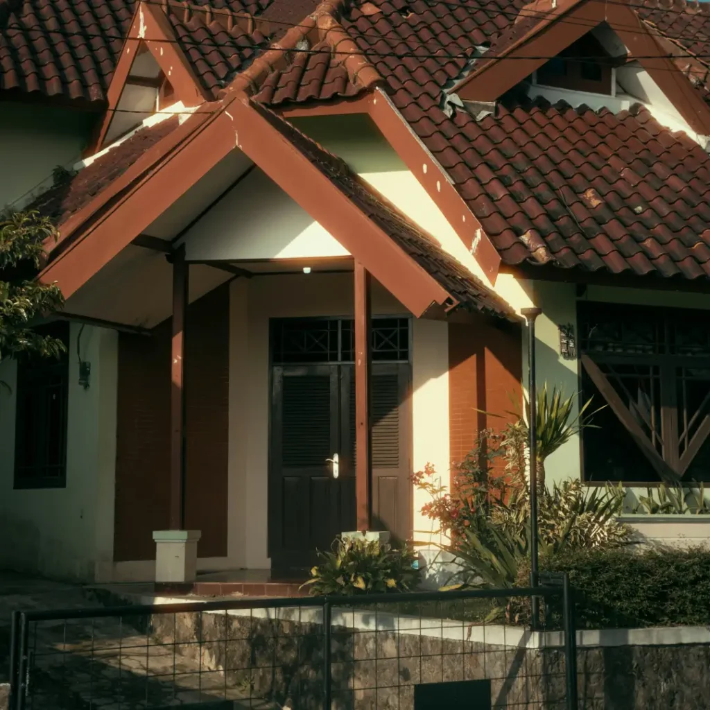 Rumah bergaya klasik dengan atap genteng cokelat, teras depan berkanopi, dan pagar besi di depannya. Gambar ini berada dalam artikel "KPR Rumah Depok" di website Ecotown.id