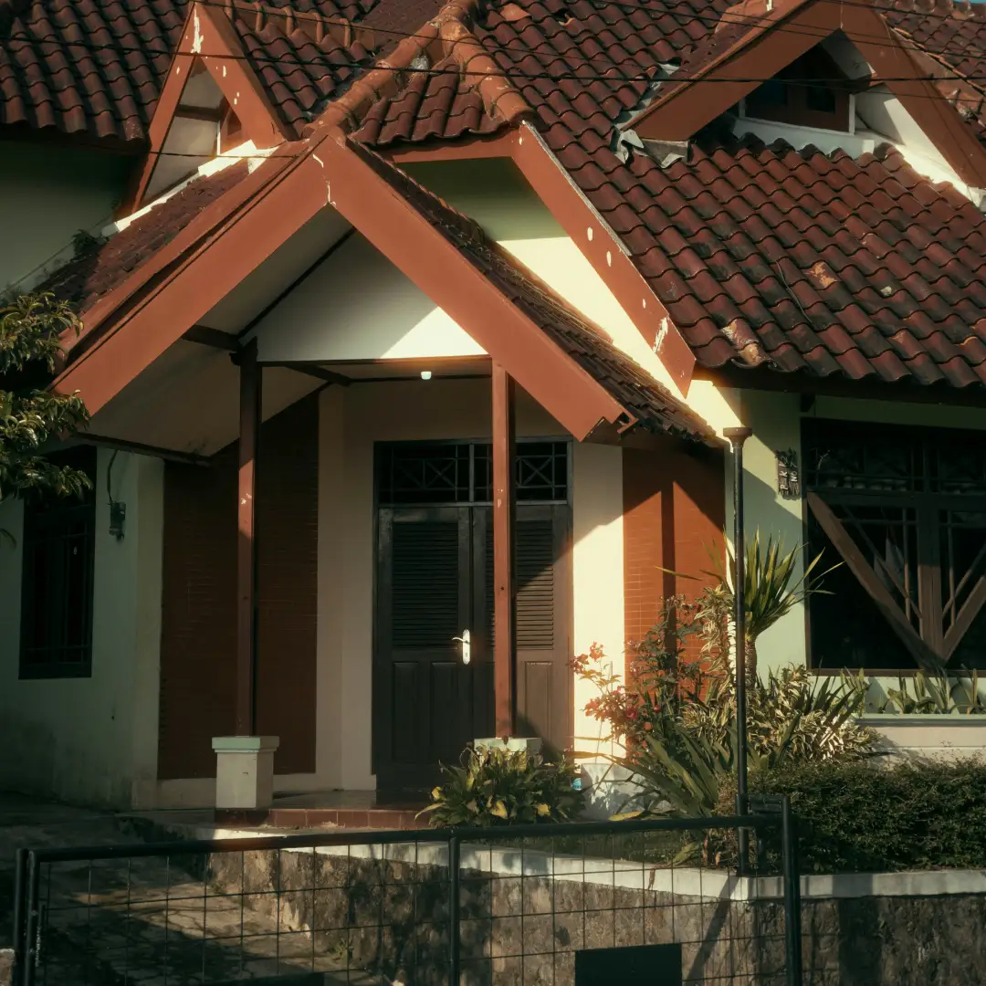 Rumah bergaya klasik dengan atap genteng cokelat, teras depan berkanopi, dan pagar besi di depannya. Gambar ini berada dalam artikel "KPR Rumah Depok" di website Ecotown.id